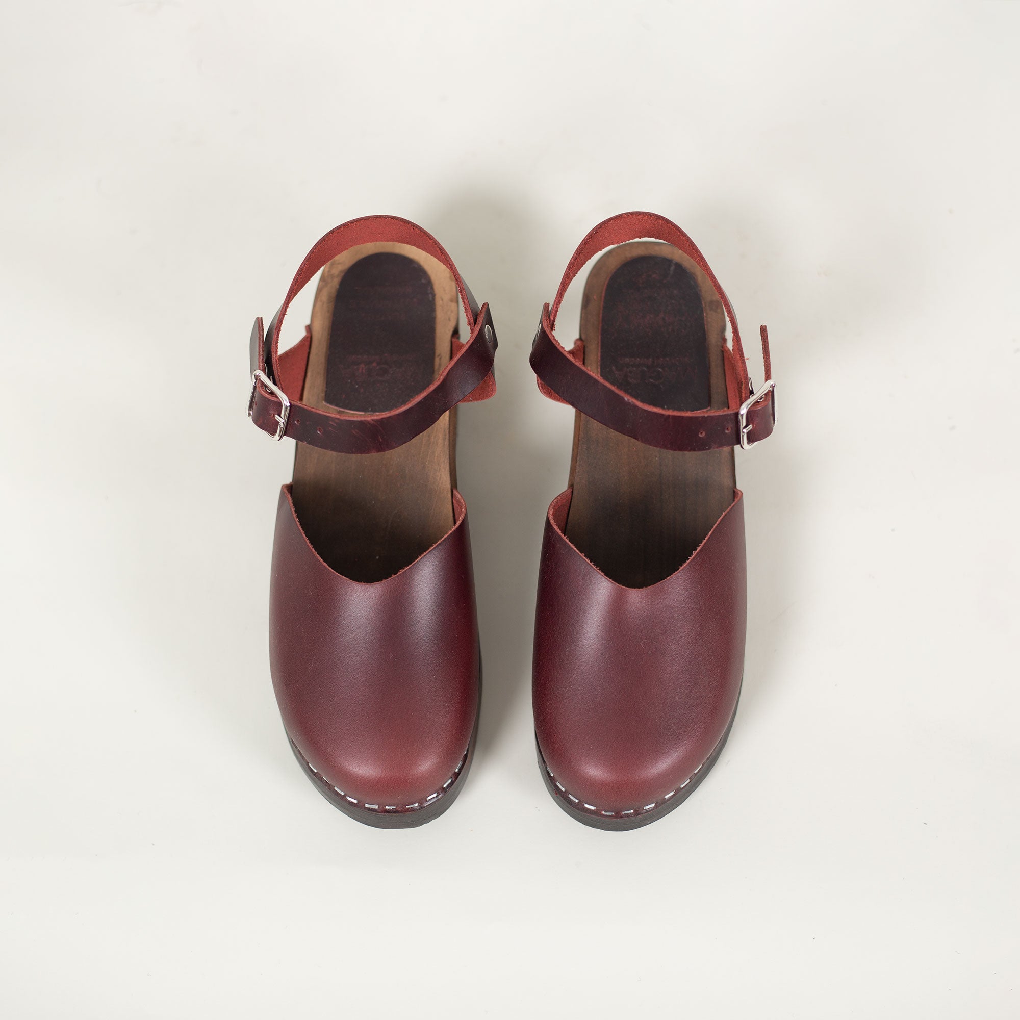 Overhead view of Swedish burgundy leather mules with low wooden heel and ankle buckle strap.