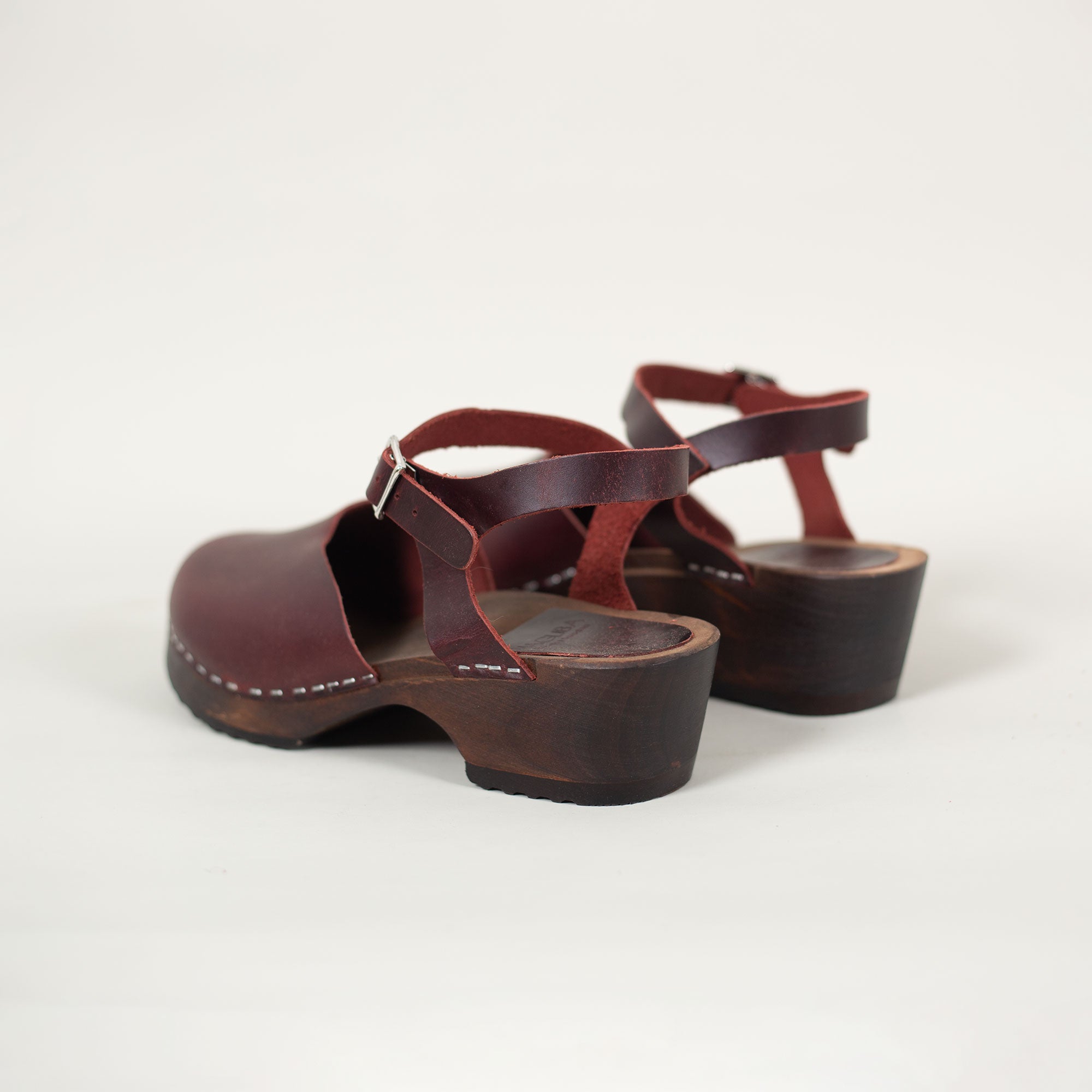 Back view of burgundy clog sandals showing wooden heel and ankle strap detail.