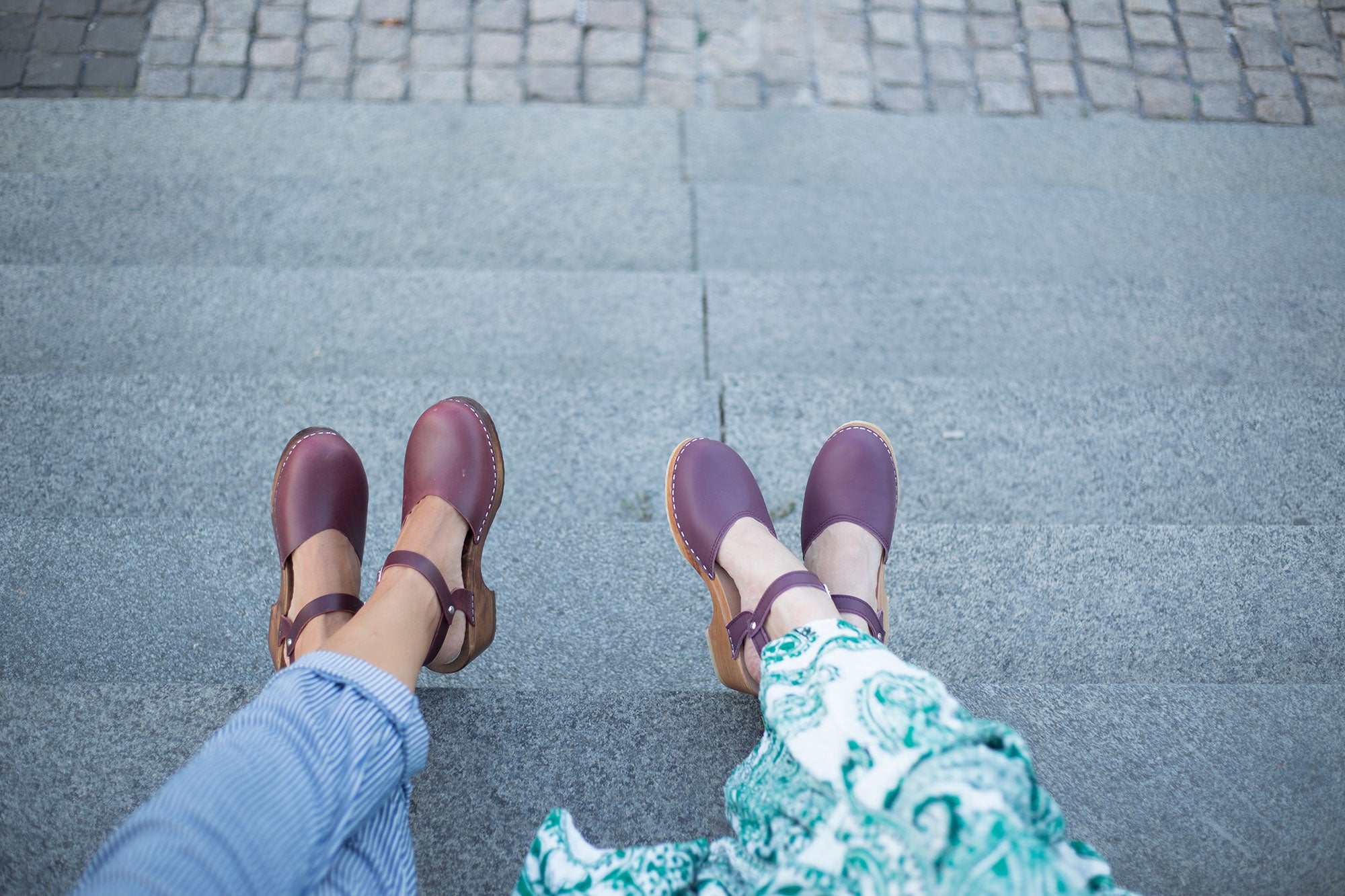 Woman wearing burgundy Swedish leather clogs with ankle strap, styled with casual outfit.